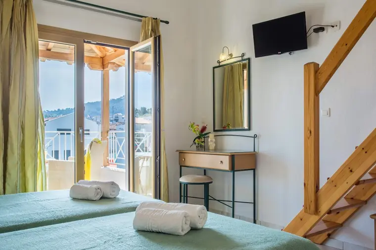 An apartment with twin beds and wooden stairs up to the loft